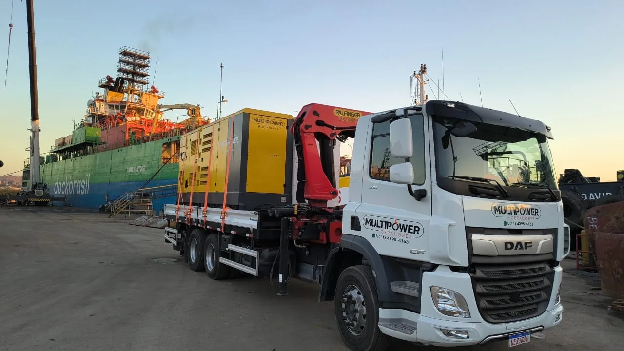Caminhão da MultiPower com gerador em área portuária junto a navio.