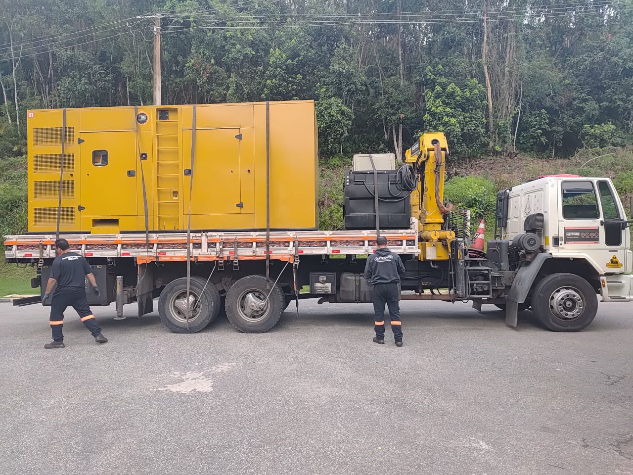 Equipe junto a caminhão transportando gerador amarelo.