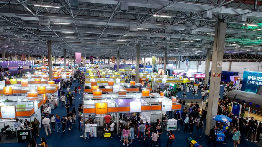 Pavilhão com estandes e visitantes em feira.