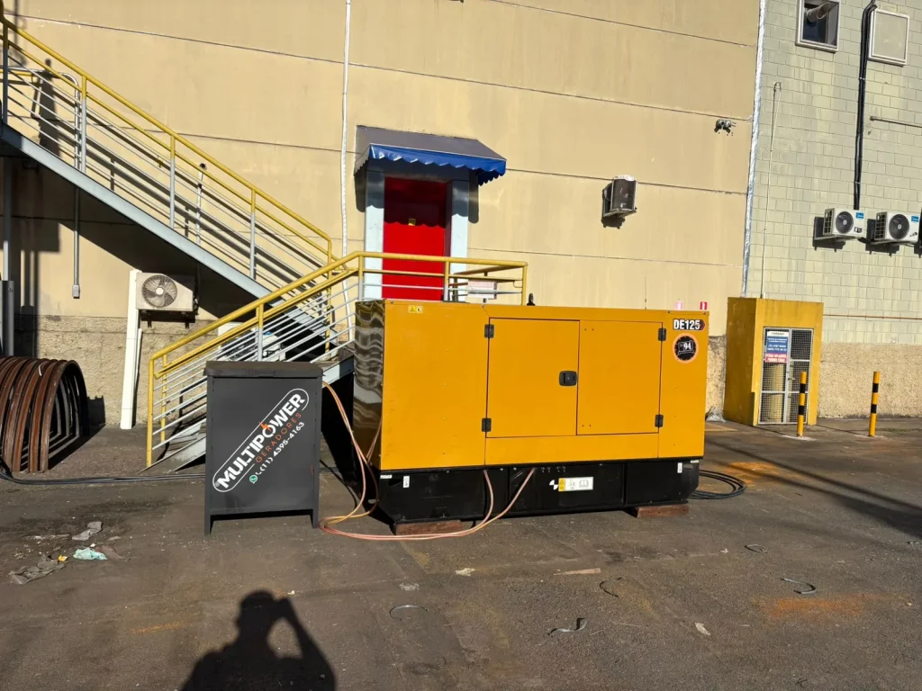 Gerador amarelo e equipamento auxiliar junto a prédio comercial.