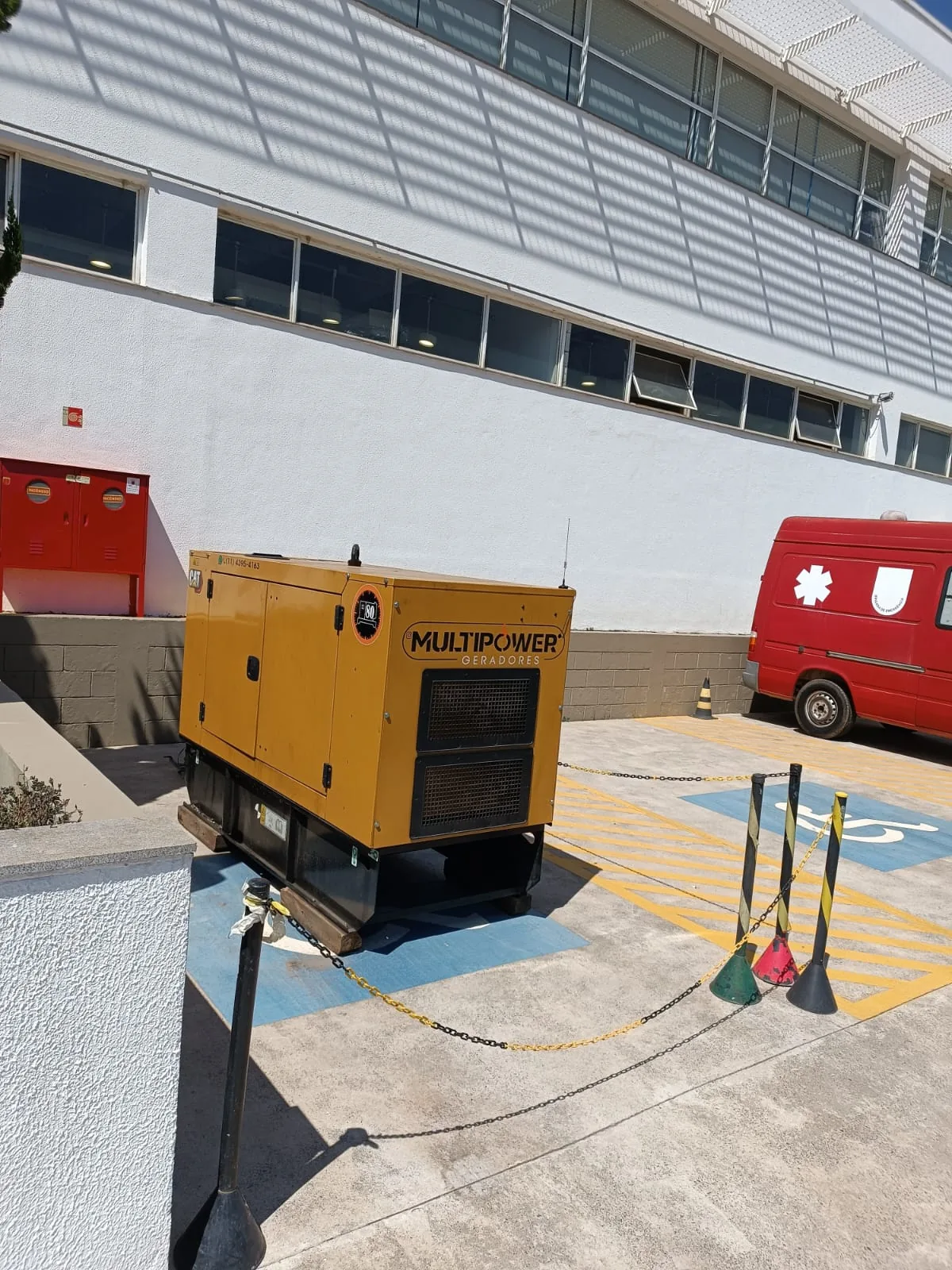 Gerador amarelo em área externa demarcada junto a edifício.