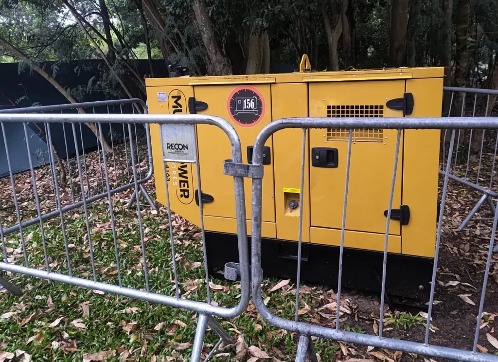 Gerador amarelo isolado por grades em área arborizada.