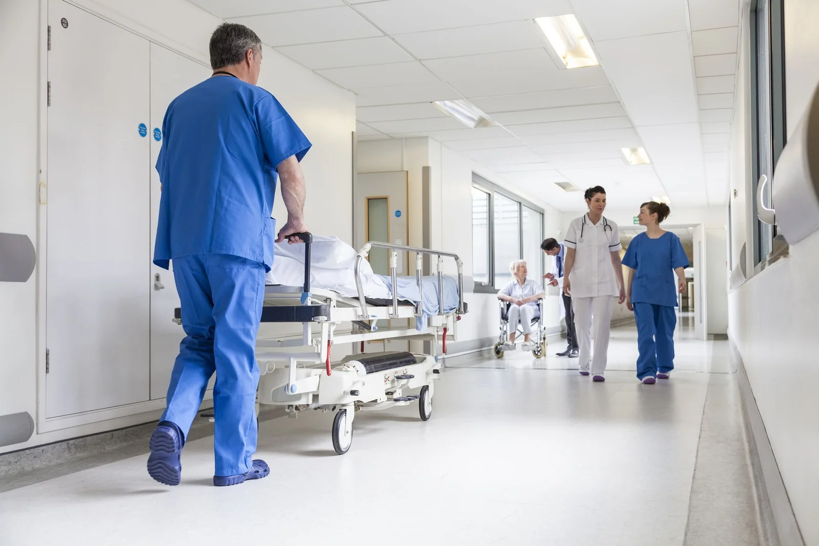 Profissionais e maca em corredor hospitalar.